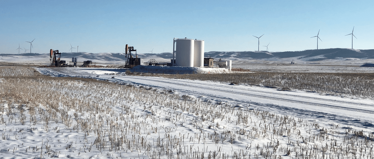 Snow covered prairie featuring wind turbines and oil extraction equipment