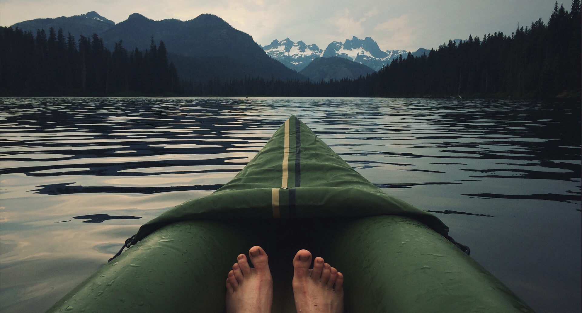 A person sits in a canoe on a lake with the mountains in the background. You can only see their feet, as the photo was taken from their perspective.