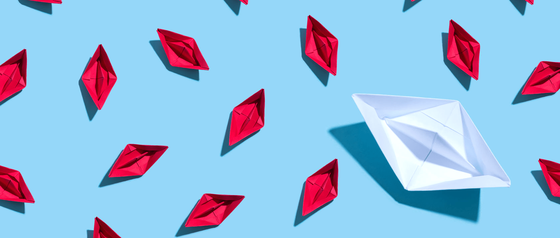 A large white paper boat stands out amongst identical tiny red boats.