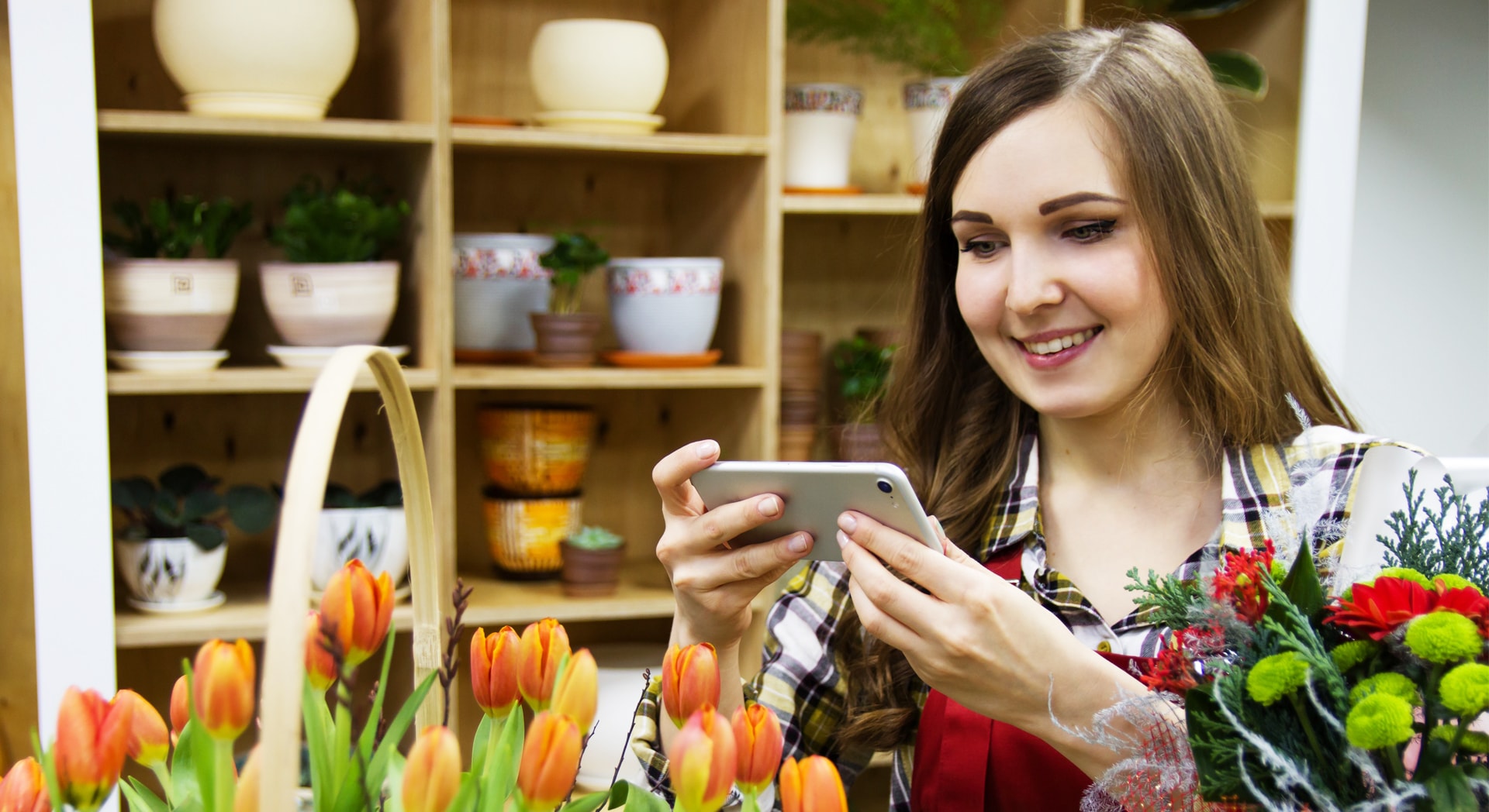 A florist smiles as she uses her phone to take photos of her flower arrangements.