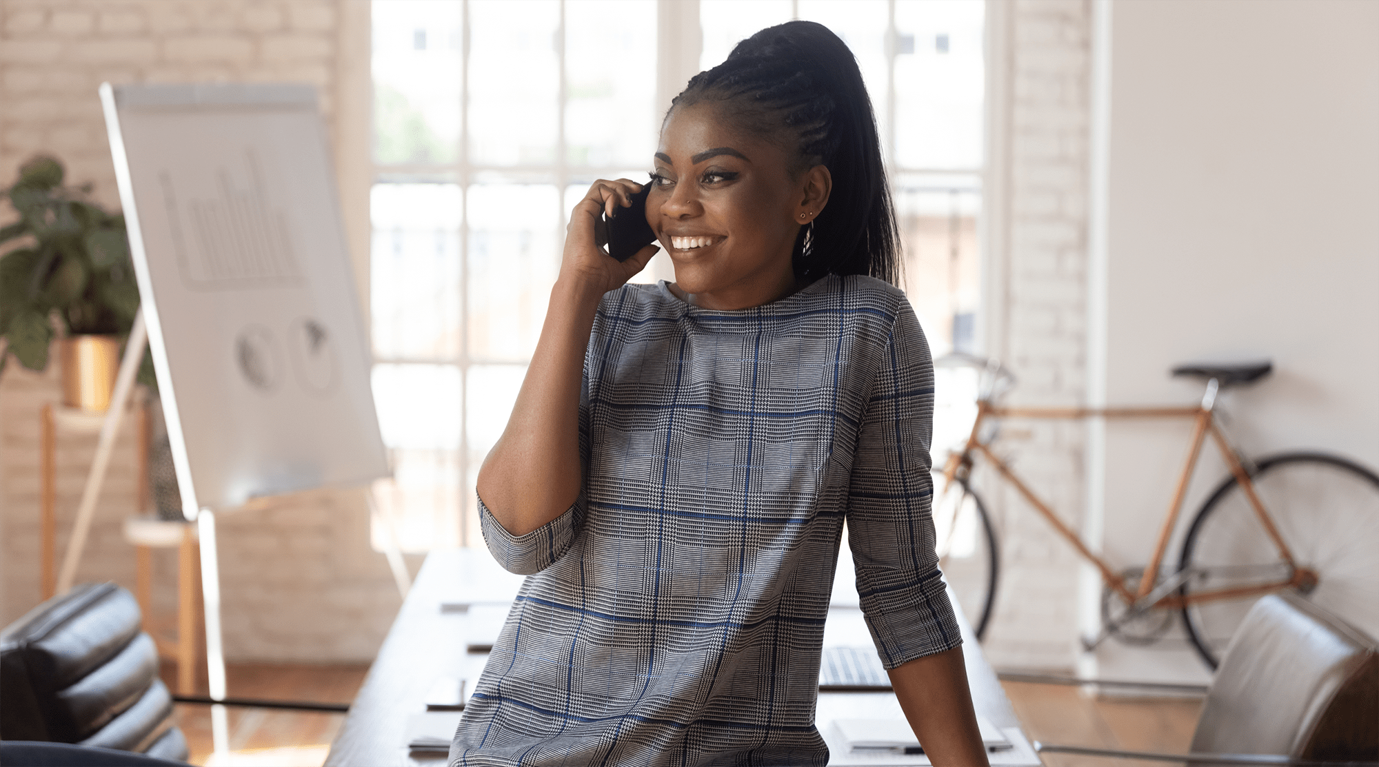 Woman leaning on a desk in her office while smiling and talking on the phone
