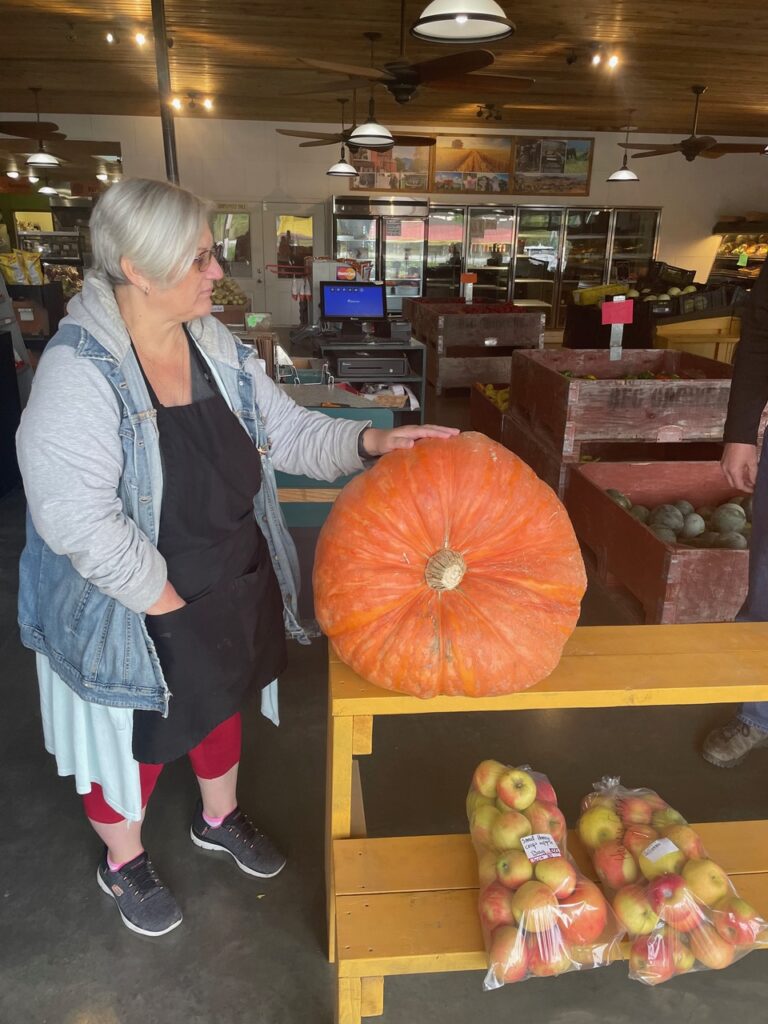 Donna, the owner at Creston Fruit Market, posing with a large pumpkin